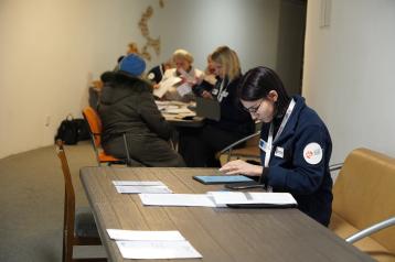 Woman sitting behind a desk with other people in the background 